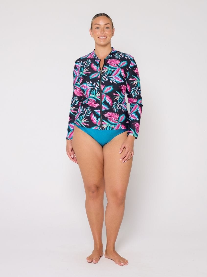 Woman wearing a colorful tropical print shirt and blue swimsuit on a white background