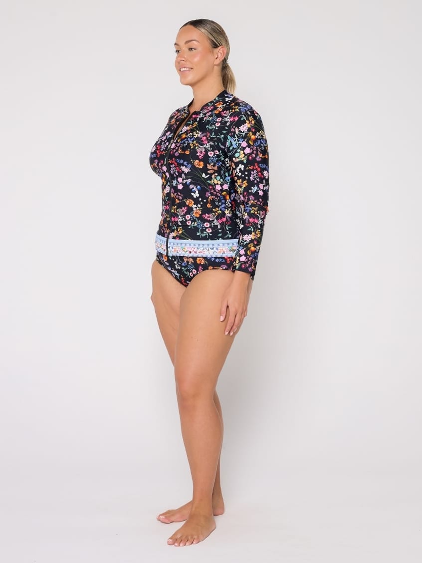 A woman modeling a long-sleeve floral swim top and matching bikini bottoms against a plain light gray studio background.