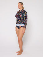 A woman modeling a long-sleeve floral swim top and matching bikini bottoms against a plain light gray studio background.