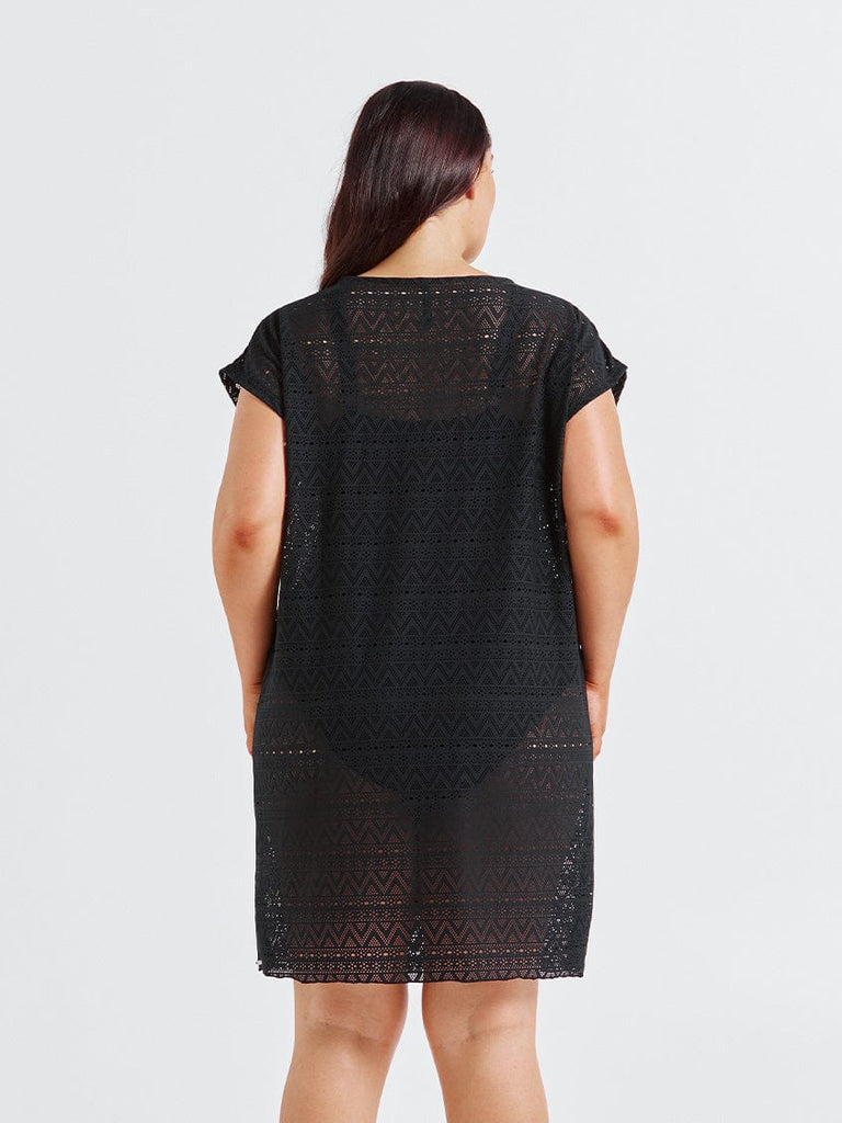 Woman in studio wearing a black patterned dress on a light gray background in studio