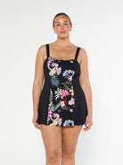 Blonde model shows the front of black floral modest pool proof swim dress with wide straps