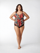 A woman modeling a ruffled tankini swimsuit with a vibrant multicolor abstract print and solid black bottoms, standing against a light gray studio background.