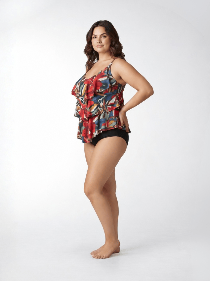 A woman modeling a sleeveless ruffled bikini top with a colorful abstract print in red, blue, yellow, and black, paired with black bikini bottoms, against a plain white studio background.