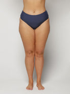 Woman wearing navy polka dot high-waisted bikini bottoms on a light gray background