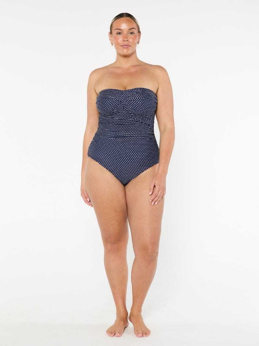 Woman wearing a strapless navy swimsuit with white polka dots on a white background