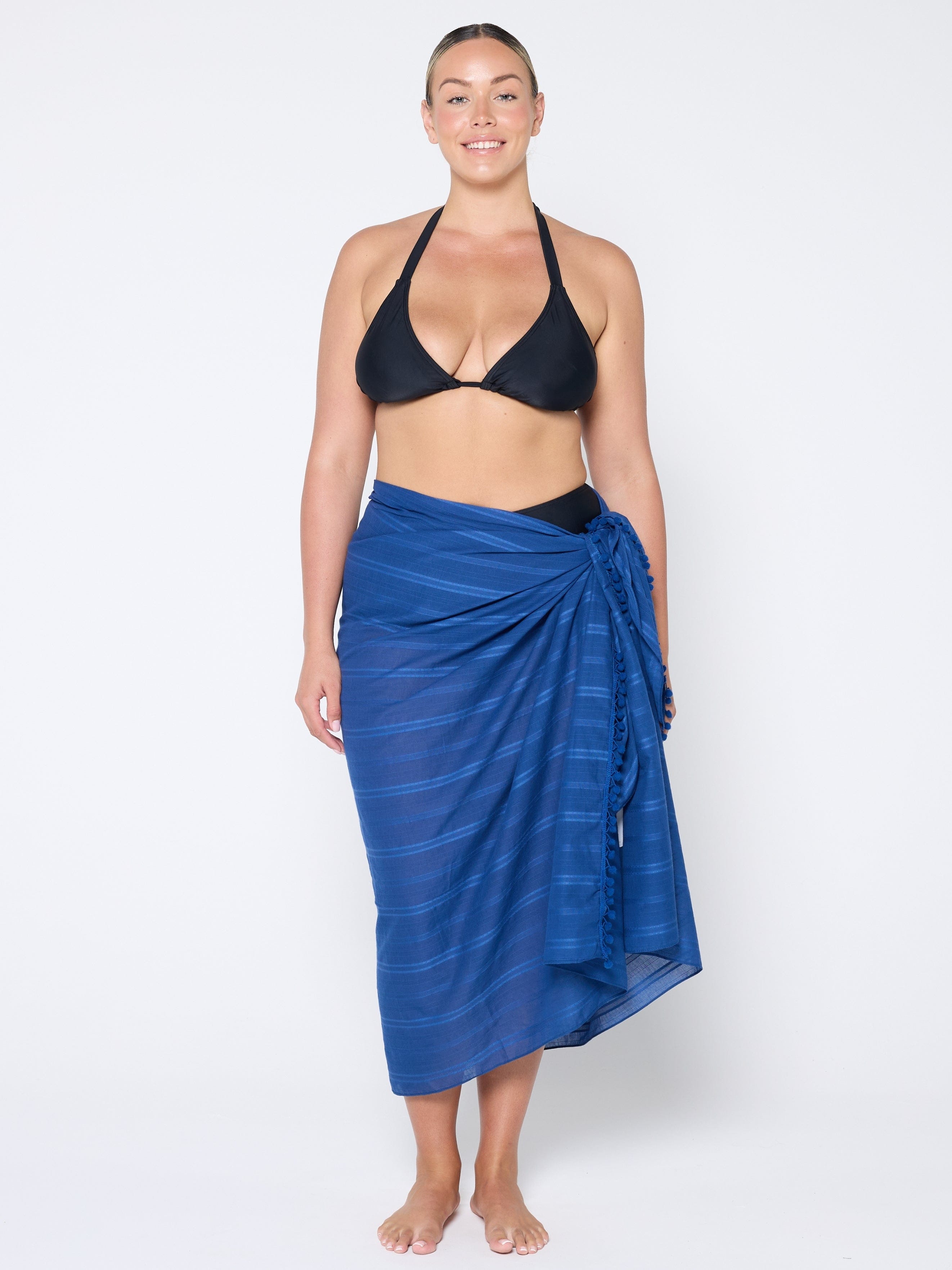 Woman wearing a black bikini top and blue striped sarong on a white background