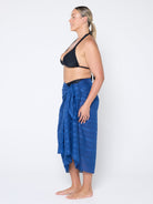 Woman wearing a blue sarong and black bikini top on a white background