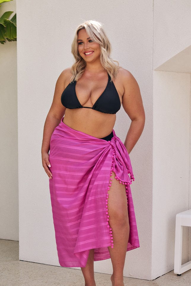 Blonde model wearing black bikini with hot pink pom pom sarong