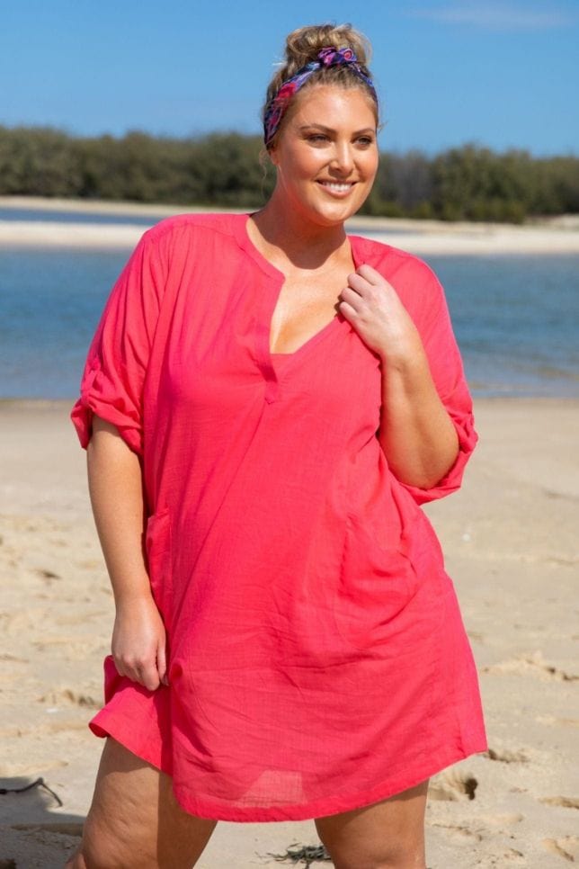 Blonde model kneeling on the beach wear a pink cotton over shirt with rolled up sleeves