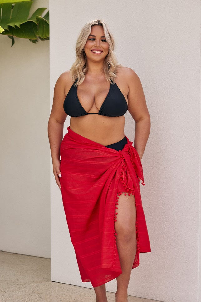 Blonde model wearing black bikini with long red sarong