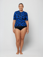 Woman wearing a blue patterned rash guard and black shorts on a white background