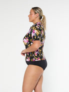 Blonde model shows the side of chlorine resistant short sleeve tropical print rash vest