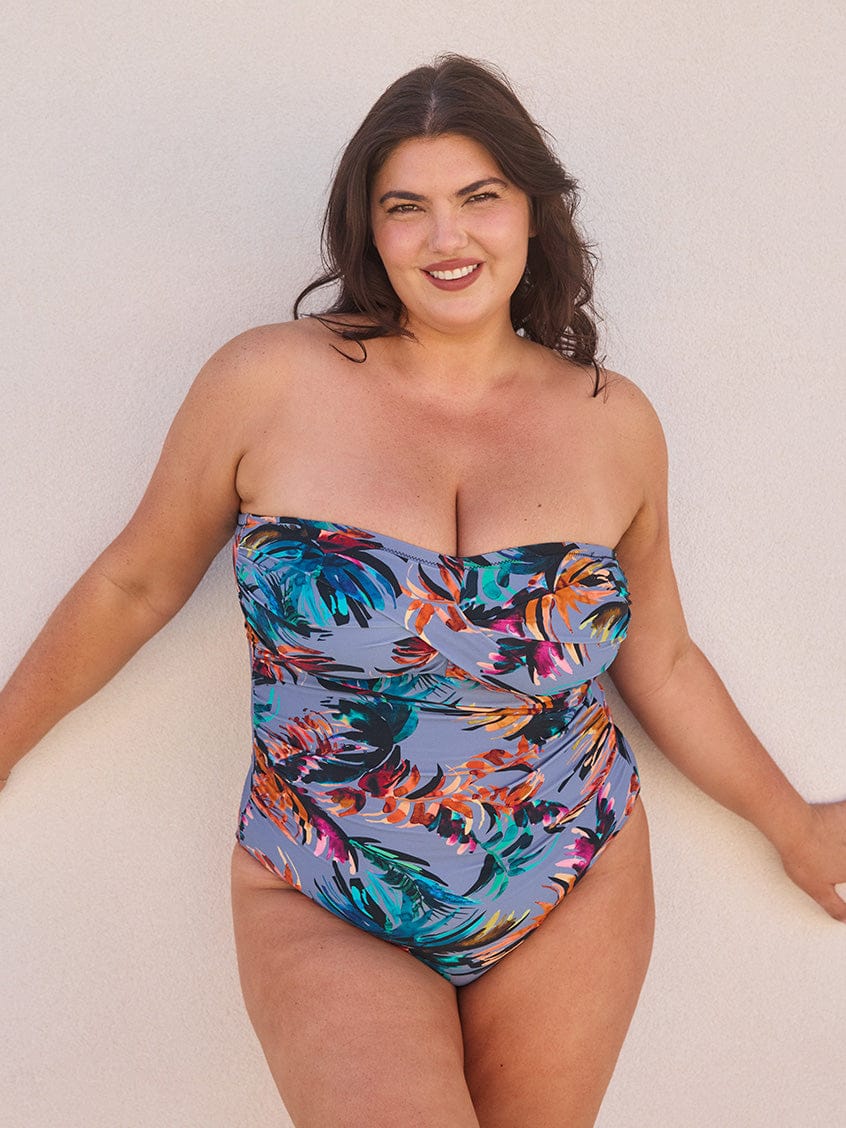 Model posing on wall wearing a grey one piece bandeau with multi coloured floral