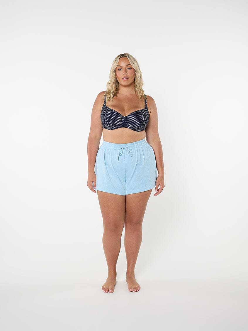 Woman wearing a navy patterned top and light blue shorts on a white background