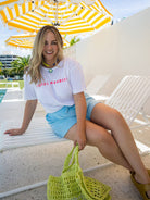 Woman sitting on a beach chair under a yellow and white striped umbrella, wearing a 'HOTEL PARADISE' t-shirt.