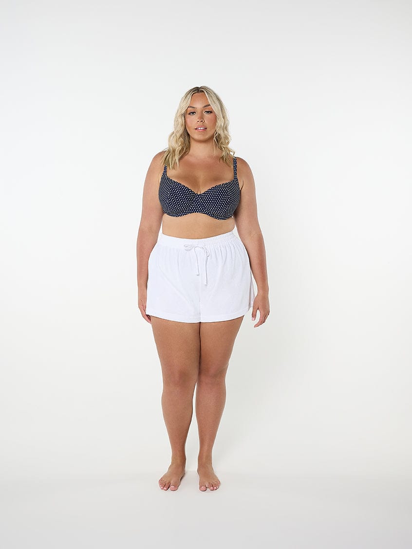 Woman wearing a navy patterned top and white shorts on a white background