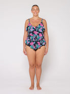 A woman modeling a 3 tier tankini with a tropical palm leaf pattern in pink, teal, and black against a plain white studio background.