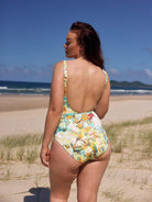 Woman in a floral swimsuit standing on a beach with ocean and sky in the background