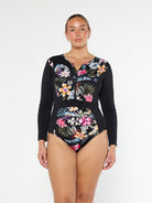 Blonde model shows the front of a floral print one piece with zip front and long sleeves