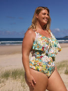 Woman in a floral swimsuit standing on a beach with ocean and sky in the background