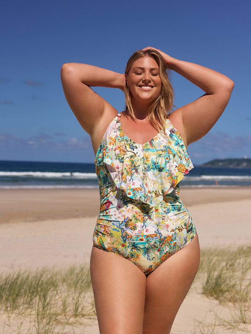 Woman in a floral swimsuit standing on a beach with ocean and sky in the background