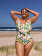 Woman in a floral swimsuit standing on a beach with ocean and sky in the background