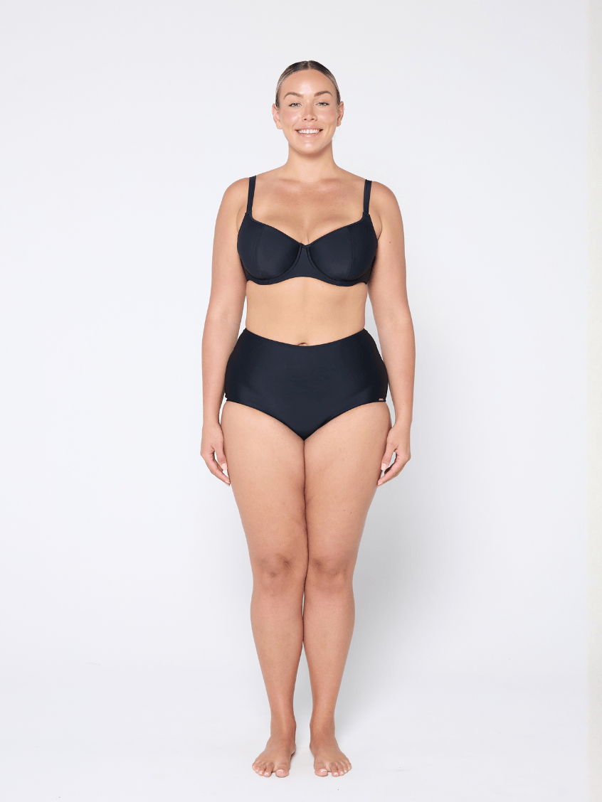 Woman wearing a black bra and high-waisted underwear on a white 