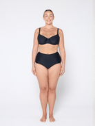 Woman wearing a black bra and high-waisted underwear on a white 