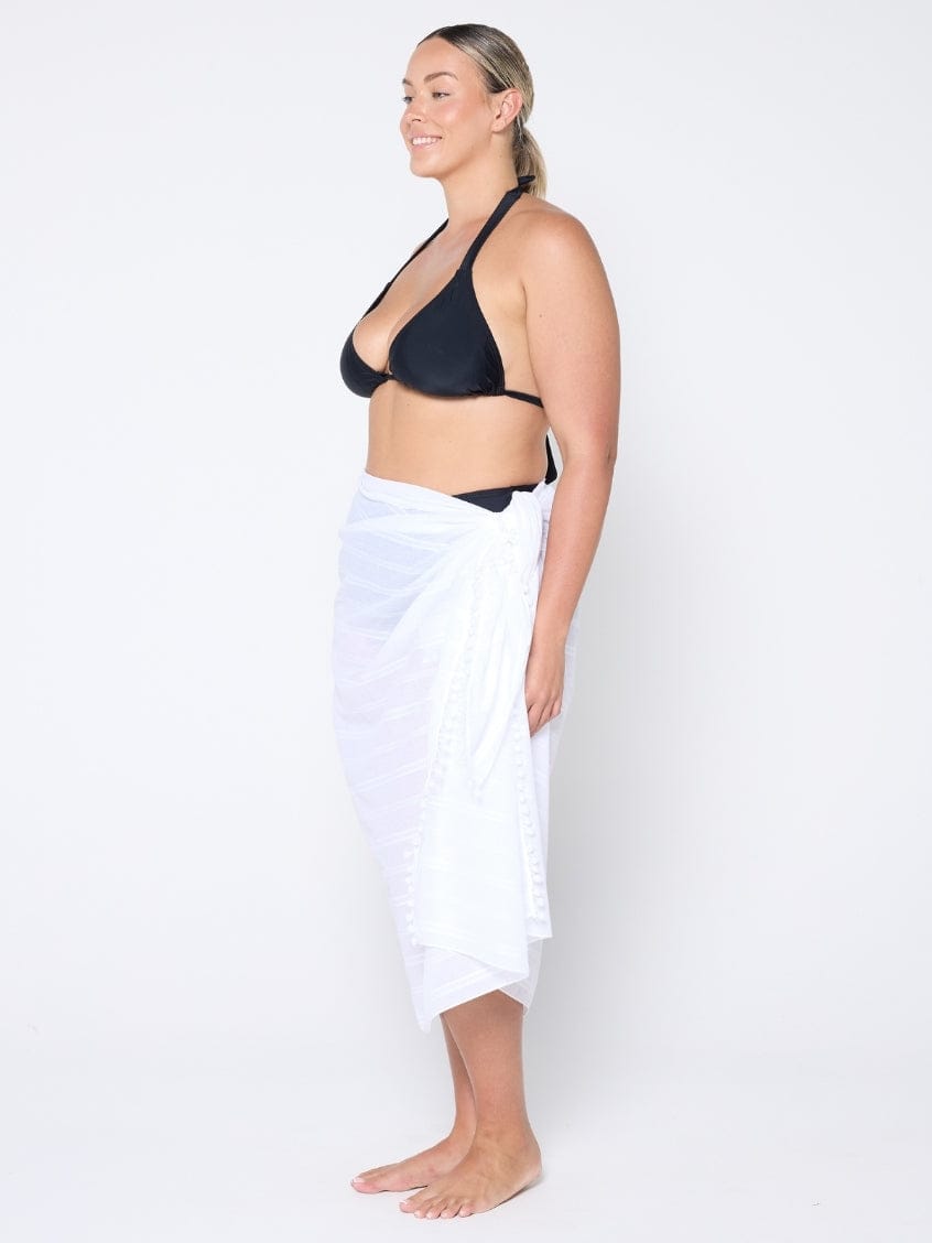 model wearing a white sarong with a black bikini top on a white wall