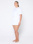 Woman wearing a white t-shirt and shorts on a plain background
