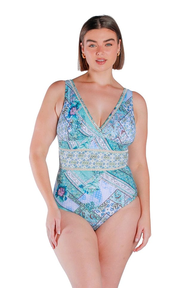 Brunette model wearing blue and white patchwork printed one piece swimsuit with v neckline