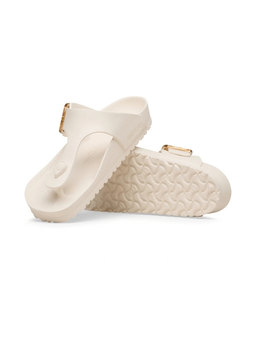 A pair of off-white double-strap slide sandals with textured soles and small gold-tone buckle details, shown on a clean white background.