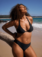 Woman in a black bikini standing on a beach with ocean and sky in the background