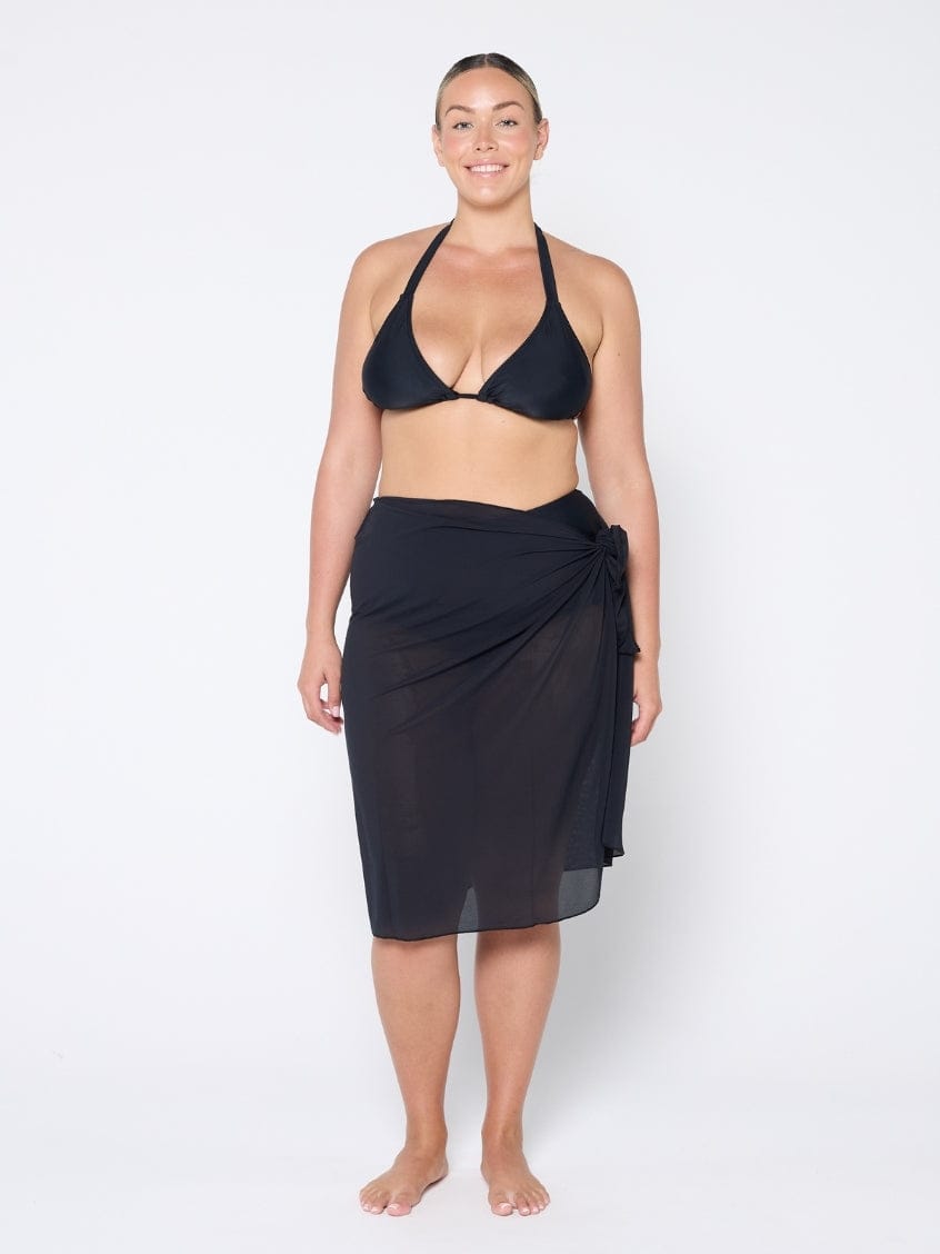 Woman wearing a black bikini and matching sarong on a white background