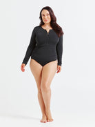Black chlorine-resistant long sleeve one piece swimsuit with zip front and UPF 50+ sun protection, shown on model standing in front of white wall
