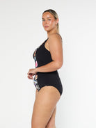 Blonde model shows the side of black and floral print one piece in chlorine resistant fabric