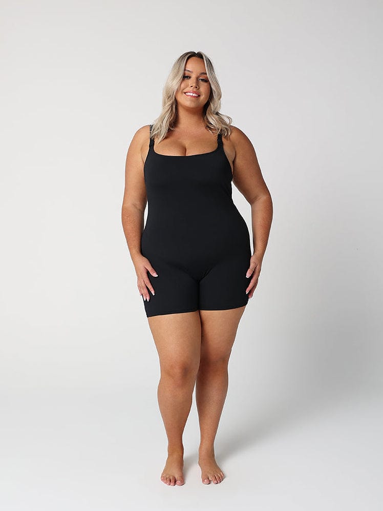 model wearing black boyleg one piece in front of a white wall