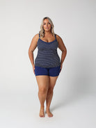 Woman wearing a navy patterned tank top and blue shorts on a white background