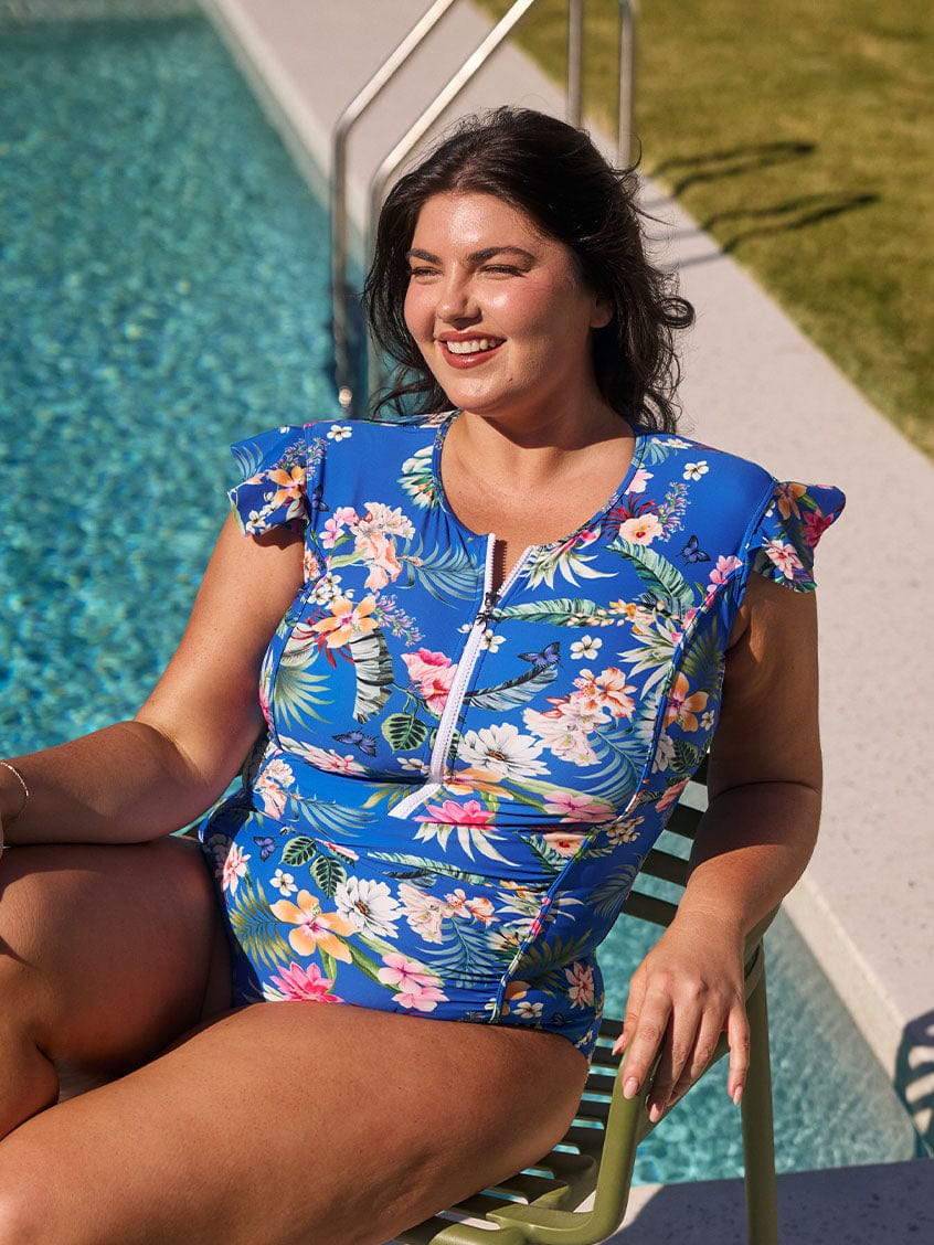 Brunette model wears blue floral ruched one piece with flattering side panels and frill sleeves