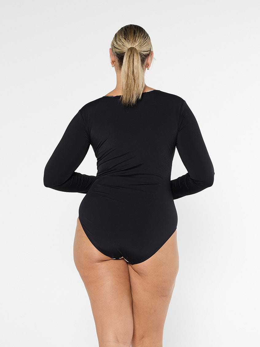 Blonde model shows the back of black chlorine resistant long sleeve one piece with full coverage bottom