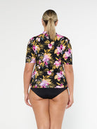 Blonde model shows the full coverage back of tropical floral short sleeve rash vest