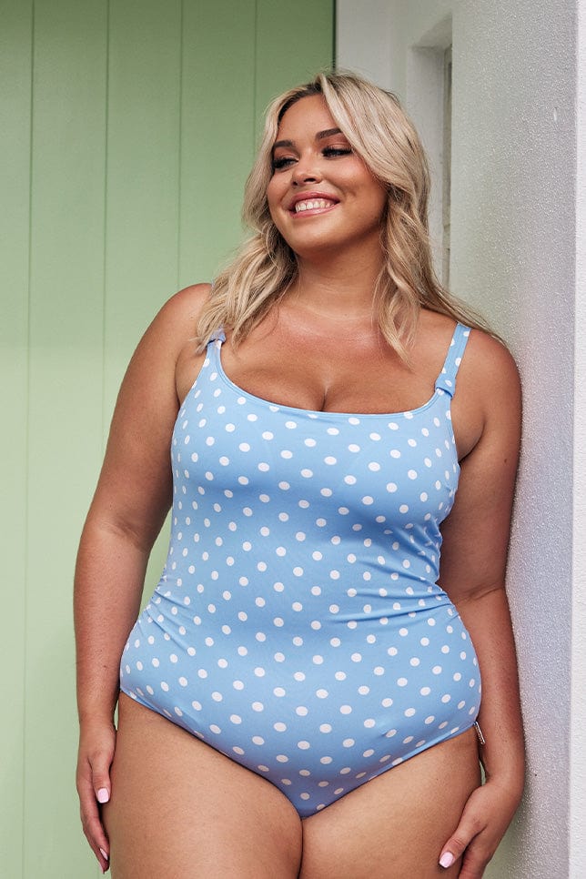 Blonde model wearing light blue with white spots one piece swimsuit