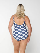 Blonde model shows the low back of navy one piece with white large polkadots