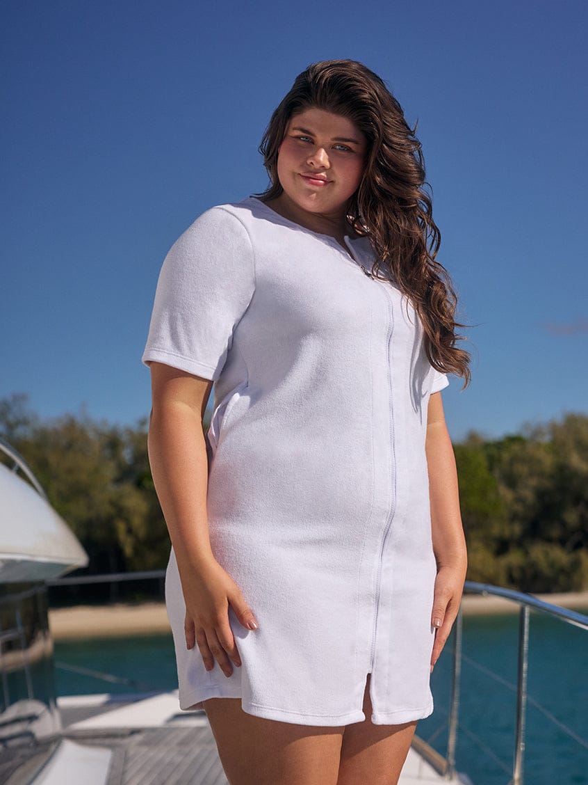 Woman wearing a white dress standing on a boat with a clear blue sky and water in the background