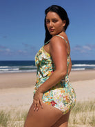 Woman in a floral swimsuit standing on a beach with ocean and sky in the background