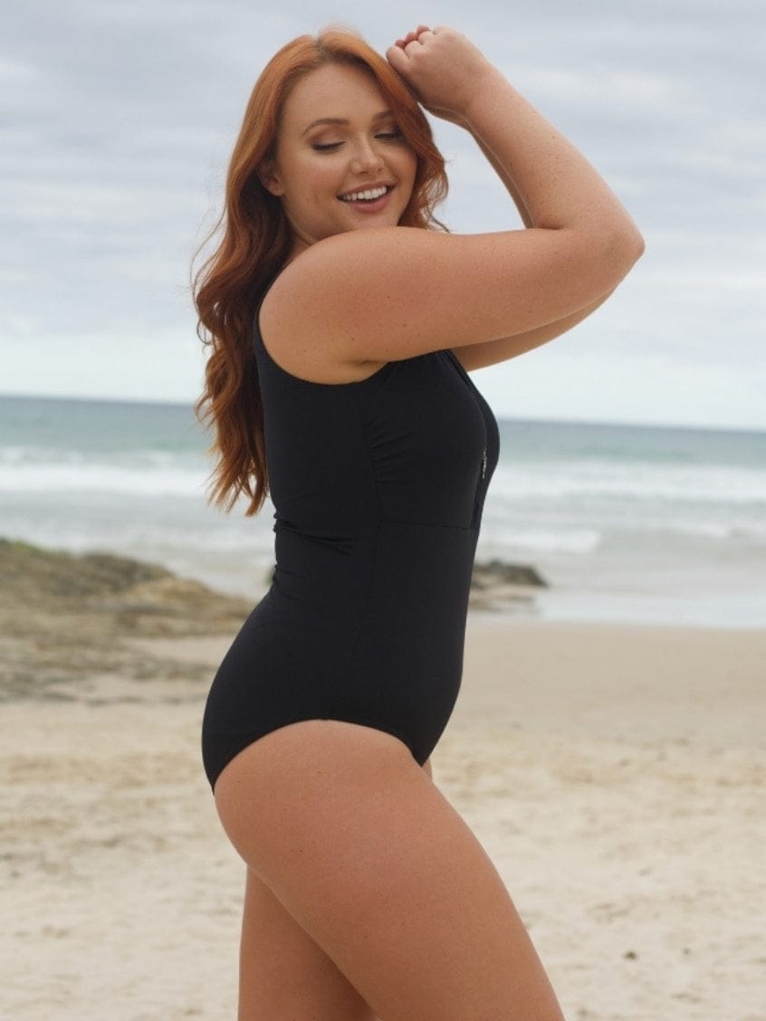 Woman in a black swimsuit standing on a beach with ocean in the background