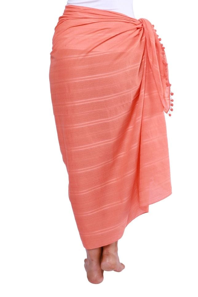 back of model wearing a coral cotton sarong tied on the side with pompom detail
