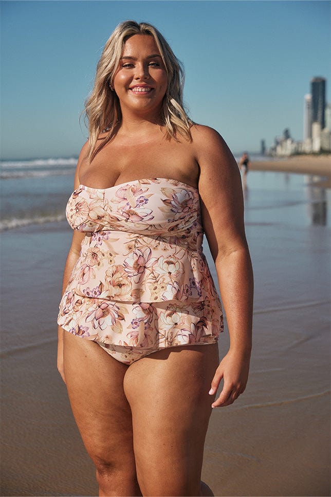 Blonde model wearing light pink floral tiered tankini top on beach