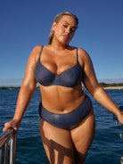 Woman in a blue polka dot bikini standing on a boat with water and sky in the background