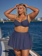 Woman wearing a navy polka dot bikini set on a boat with water and sky in the background